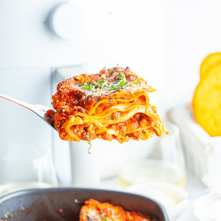 Serving spoon lifting a slice of air fried lasagna directly out of the air fryer basket