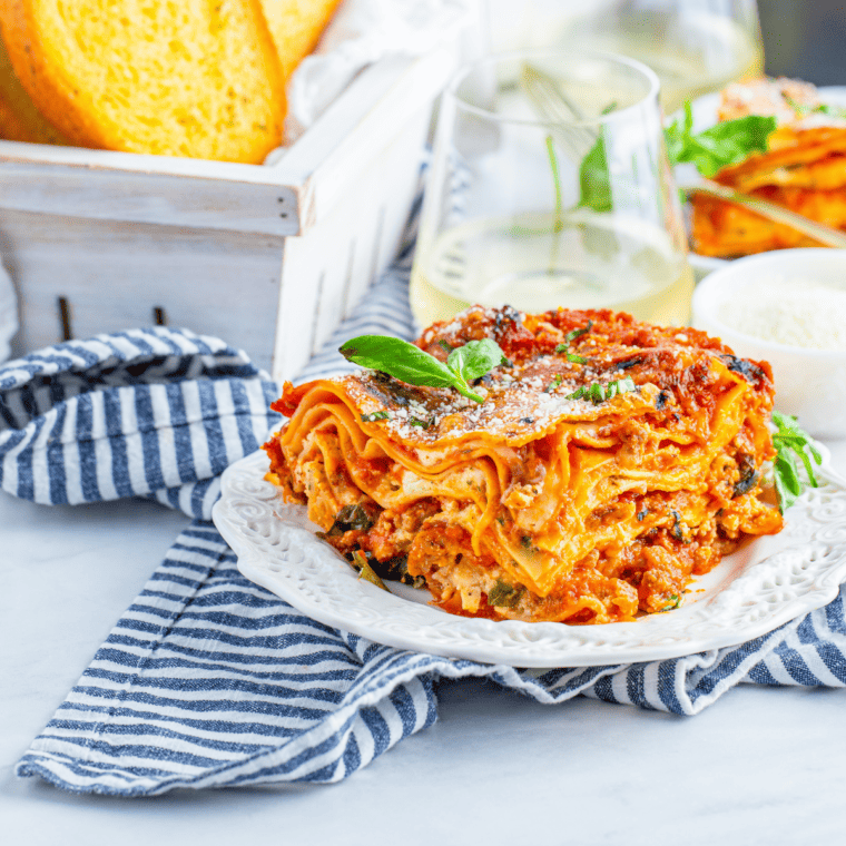 Slice of easy air fryer lasagna on a white plate served with a basket of garlic bread on the side