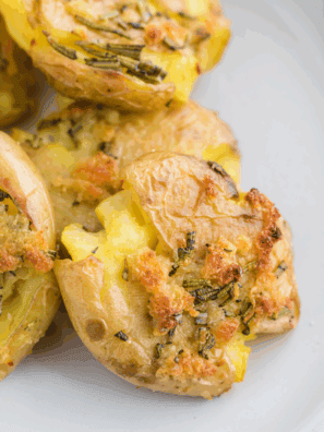Golden, crispy fried smashed potatoes served on a plate, garnished with herbs.