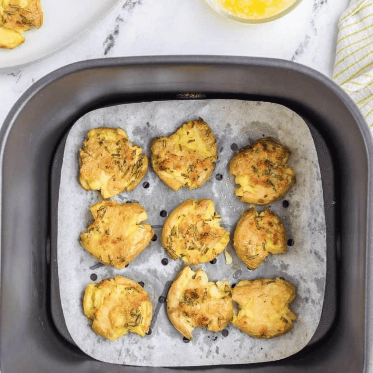 Seasoning smashed potatoes with olive oil, rosemary, garlic, salt, and pepper.