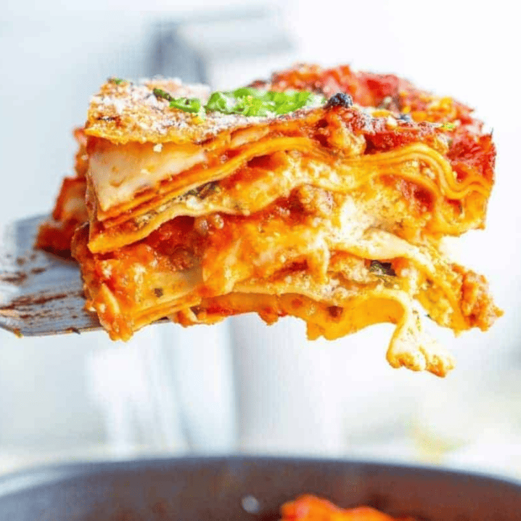 Serving spoon lifting a thick layered slice of air fryer lasagna with melted mozzarella and meat sauce
