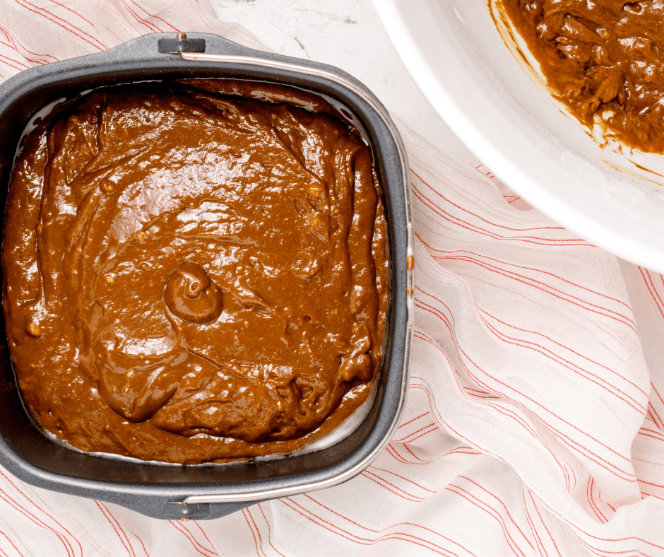 Spraying a baking pan with olive oil spray and pouring gingerbread cake batter into the prepared pan.
