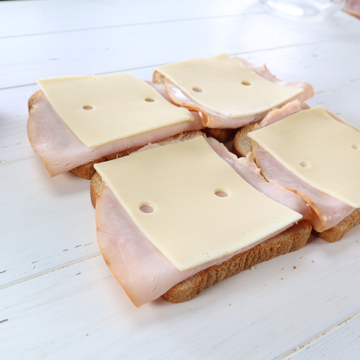 Assembling Monte Cristo sandwich with turkey, Swiss, ham, and American cheese between bread slices