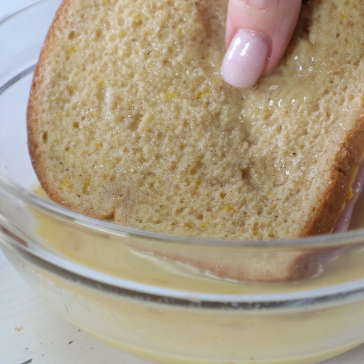 Dipping Monte Cristo sandwiches into egg, milk, salt, and nutmeg mixture
