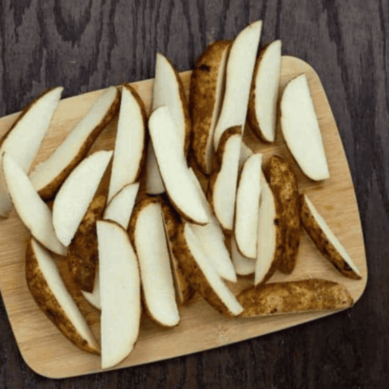 Sliced potato wedges with milk and egg in one bowl, and seasoned flour mixture in another, ready for coating.