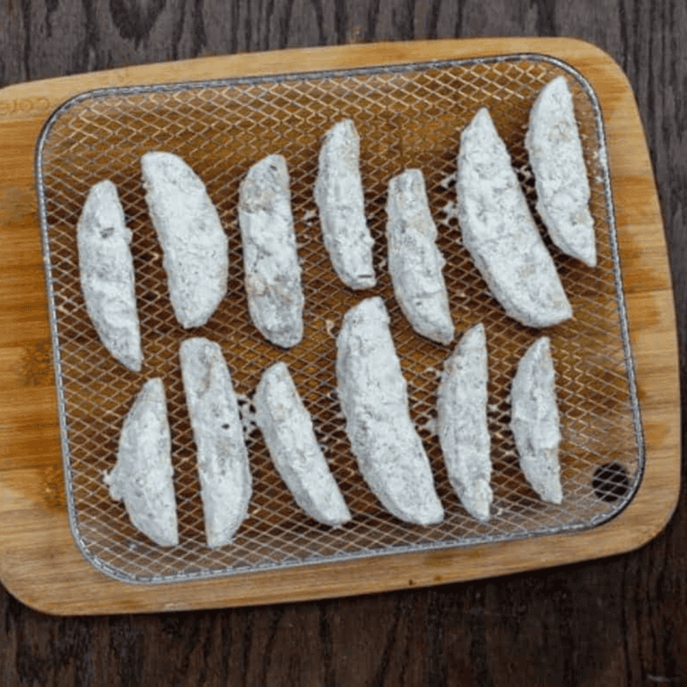Coated potato wedges being placed into a sprayed air fryer basket, ensuring they are not overcrowded.