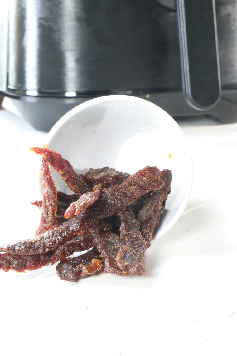 Close-up of chewy air fryer beef jerky showing meat fibers, cracked black pepper, and a tender bend in the strip