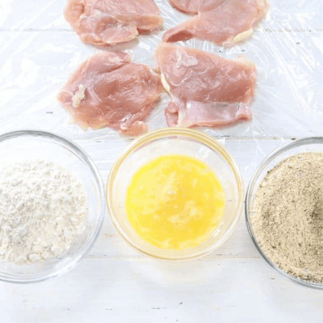 Three-bowl breading station with flour, beaten egg, and seasoned breadcrumbs for chicken thigh schnitzel
