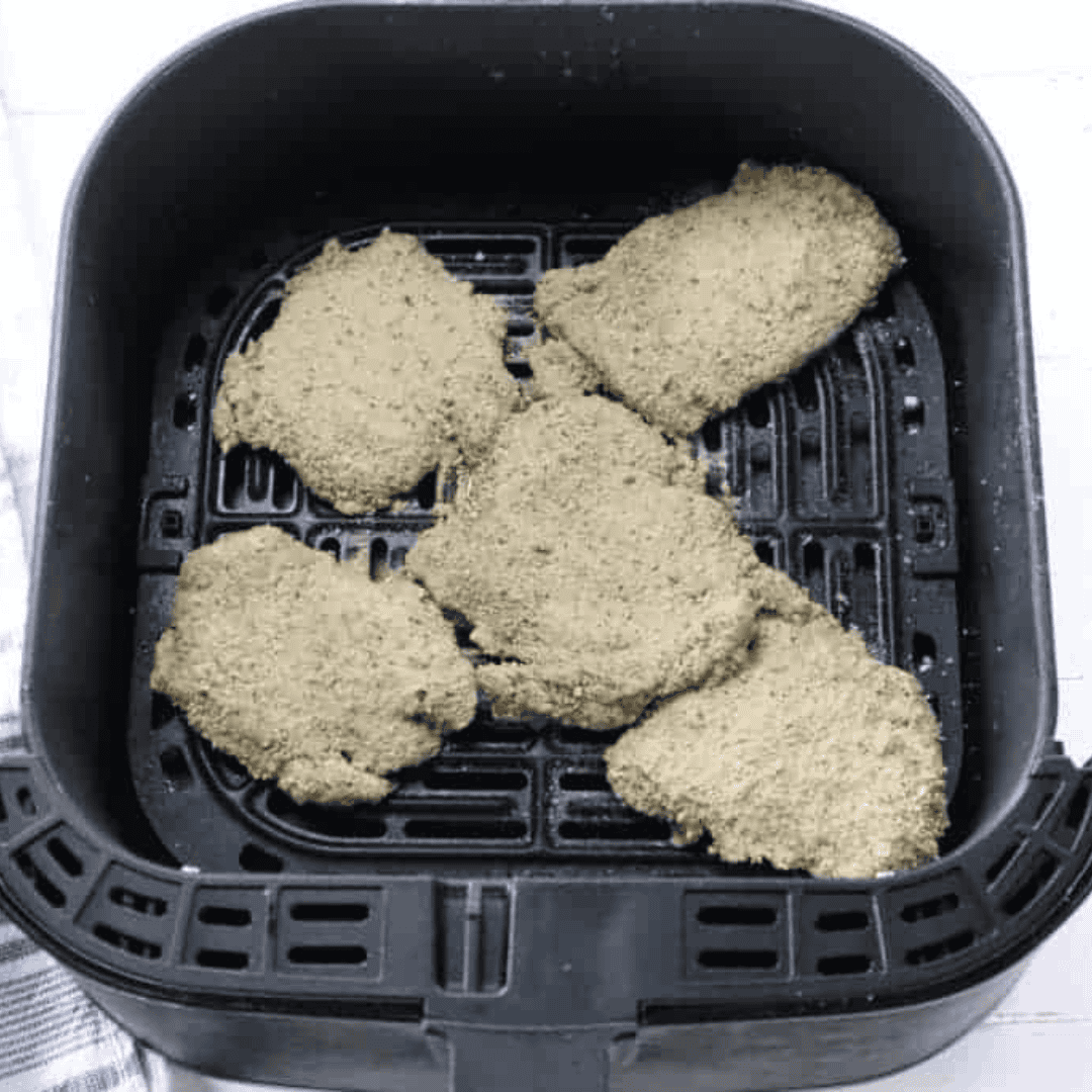 Breaded chicken thigh schnitzel arranged in a single layer in the air fryer basket