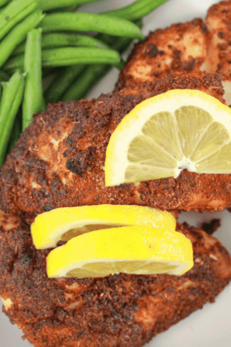 Air fryer red snapper fillet, golden and flaky, served with lemon and fresh herbs on a plate