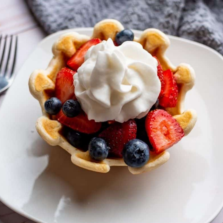 Crispy air fryer waffle bowl filled with whipped cream and fresh fruit, served on a plate.