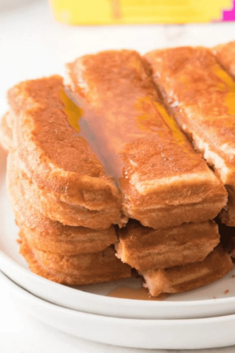 Maple syrup being poured over a stack of golden Eggo French Toast Sticks on a white plate