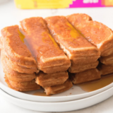 Golden Eggo French Toast Sticks stacked on a white plate with maple syrup being drizzled over the top