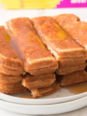 Golden Eggo French Toast Sticks stacked on a white plate with maple syrup being drizzled over the top