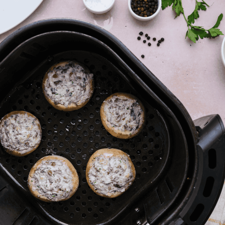 Stuffed mushrooms arranged in a single layer in the air fryer basket, cooking at 375°F until golden brown and tender.