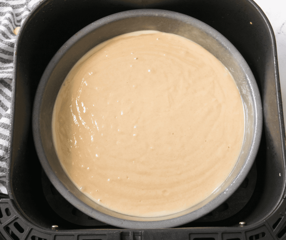 Spraying an air fryer-safe cake pan with non-stick cooking spray before baking vanilla cake.