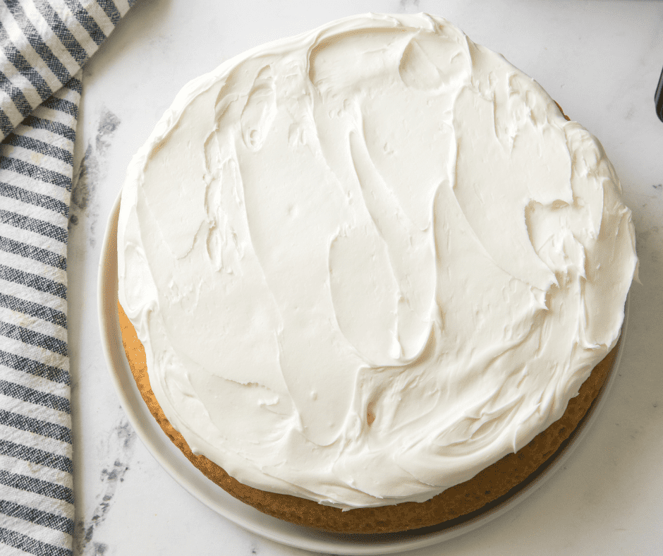 Frosted air fryer vanilla cake on cutting board.
