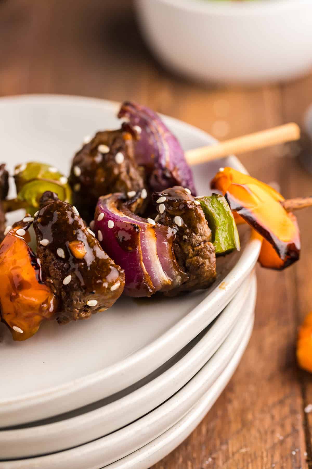 Close up of a cooked air fryer steak kabob with teriyaki sauce on top of a pile of white plates.