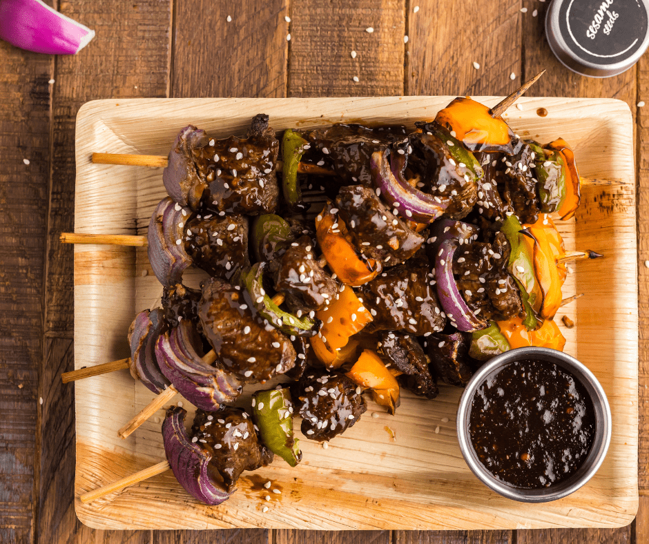 Top view of Air Fryer Cooked Beef Kabobs stacked on a rectangle plate with teriyaki sauce on the side.