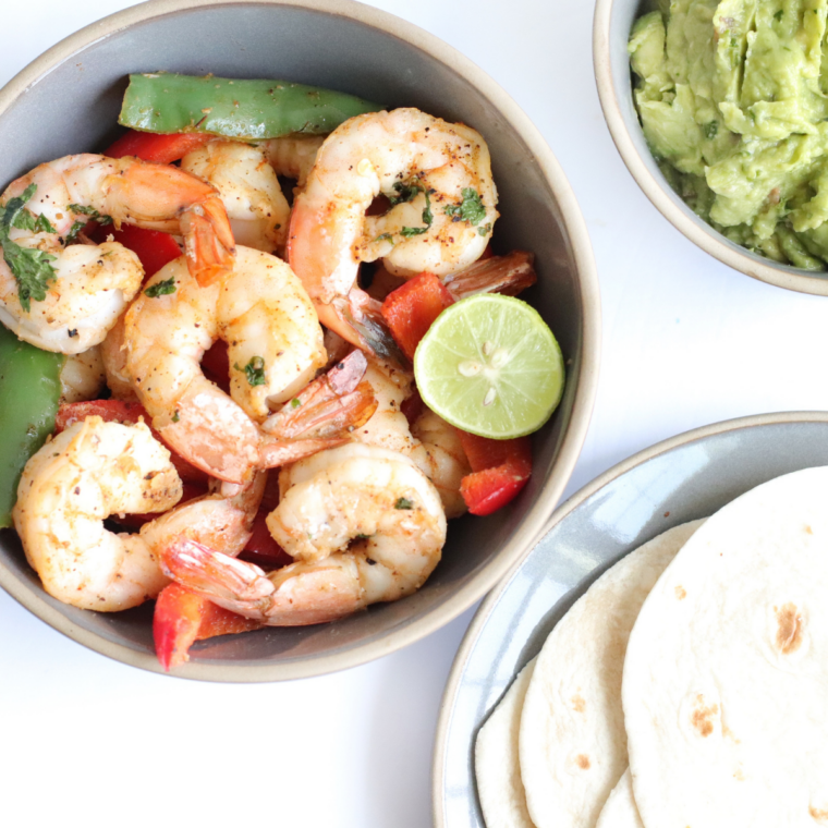 Air fryer basket filled with charred red, yellow, and green bell pepper strips with red onion, seasoned with homemade fajita spices.