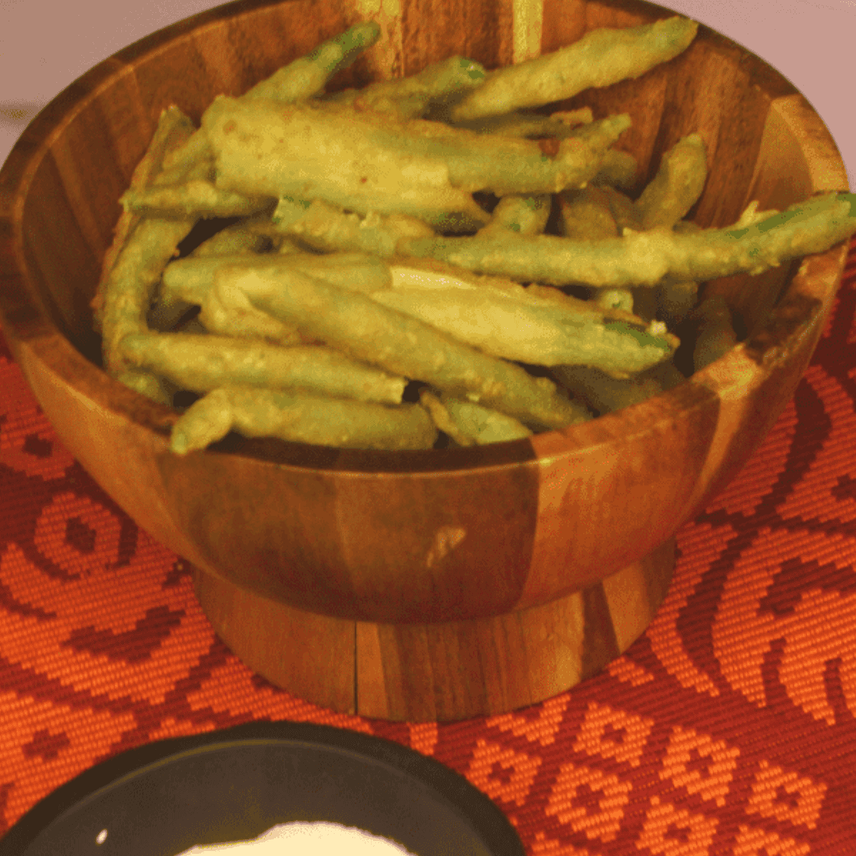Golden, crispy breaded green beans fresh from the air fryer, served on a plate with dipping sauce.