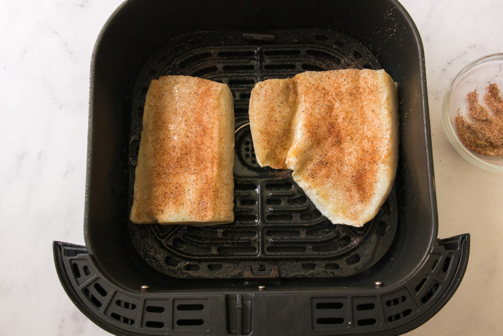 Seasoned halibut fillets placed in the air fryer basket, ready to cook at 350°F for 7-9 minutes until they flake easily with a fork.