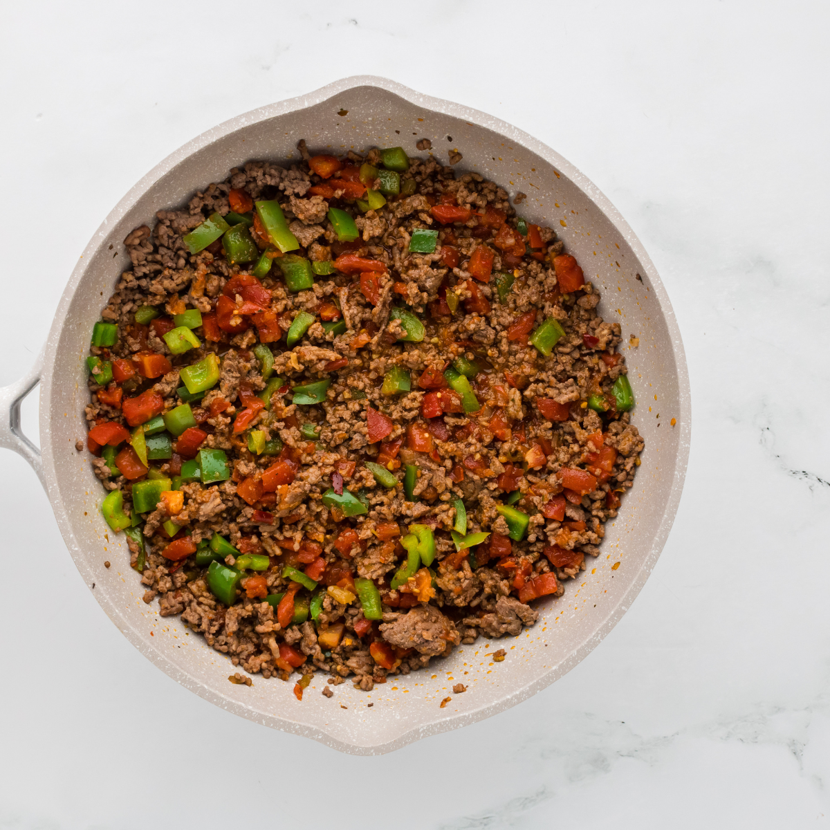Ground beef browning in skillet with bell peppers, tomatoes, and taco seasoning.