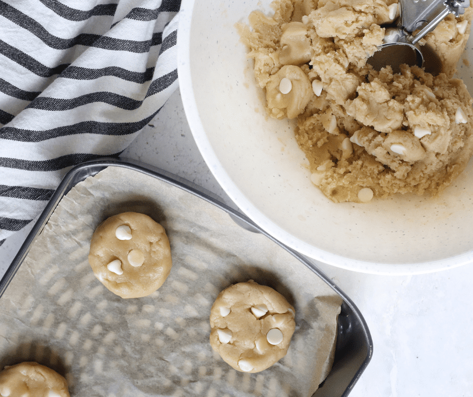 Scoops of lemon cookie dough placed on parchment paper in the air fryer basket, spaced apart for baking.