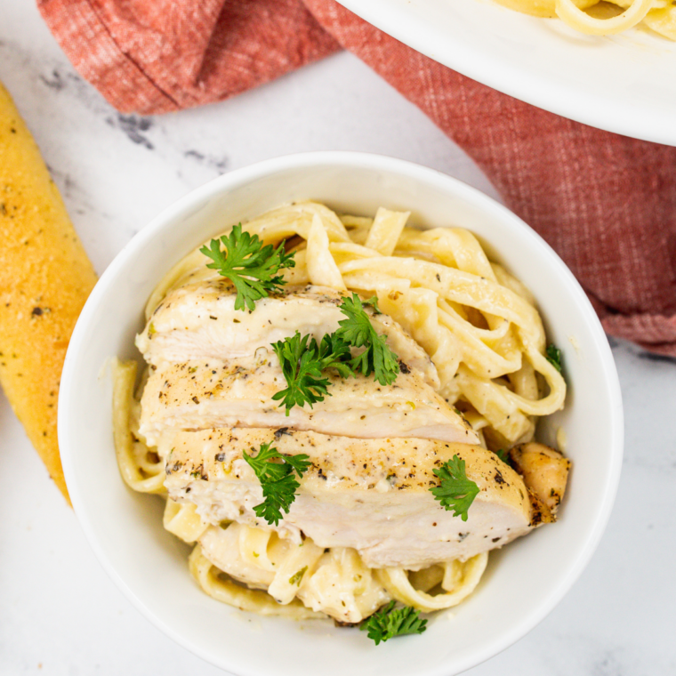 Plated fettuccine Alfredo topped with sliced chicken, Parmesan, and parsley.