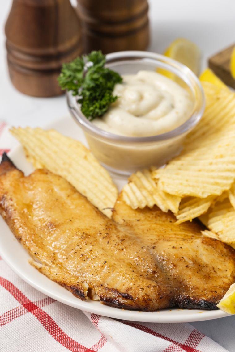 Flaky air fryer walleye fillet with no breading served on a plate with lemon slices and fresh herbs.