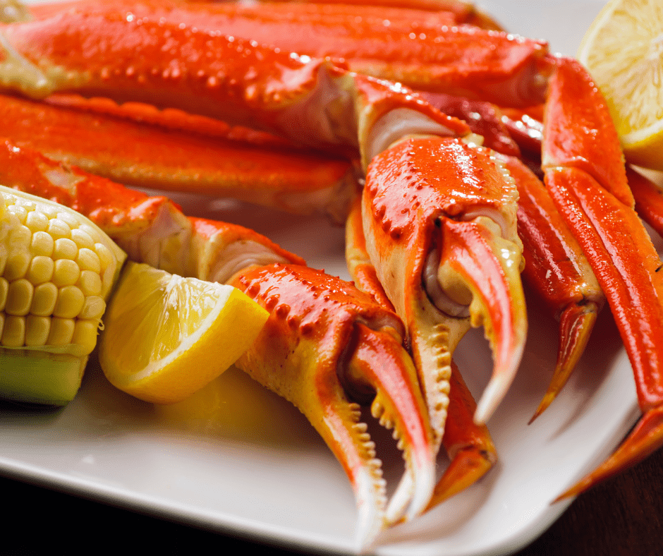 Crab legs on a white plate with corn on the cob and a lemon wedge.