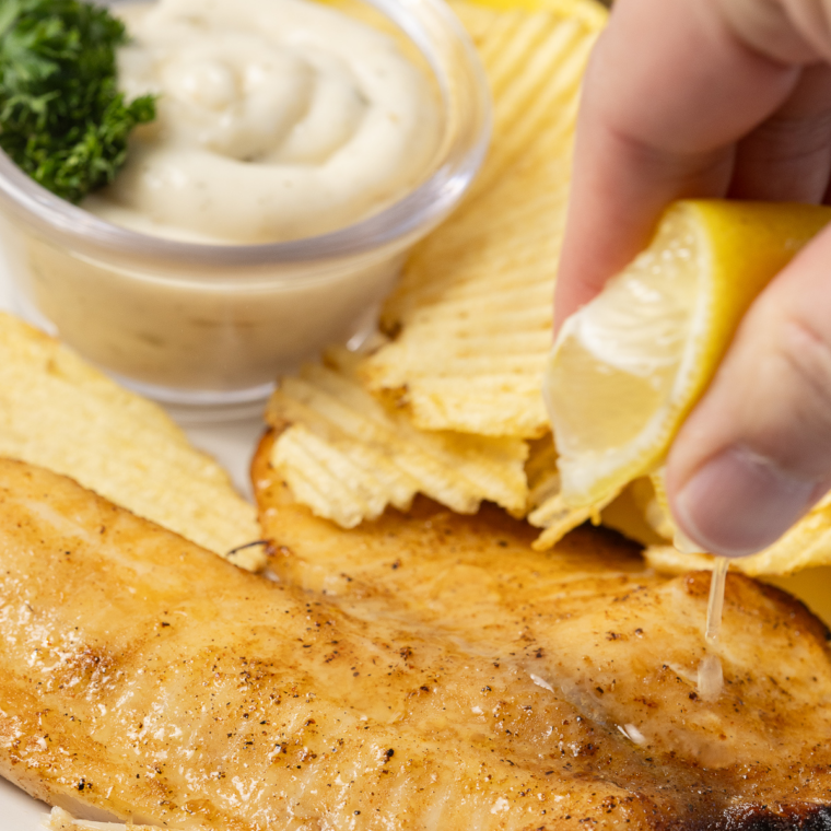 Golden air fryer walleye fillets with no breading served on a plate with lemon wedges and fresh herbs