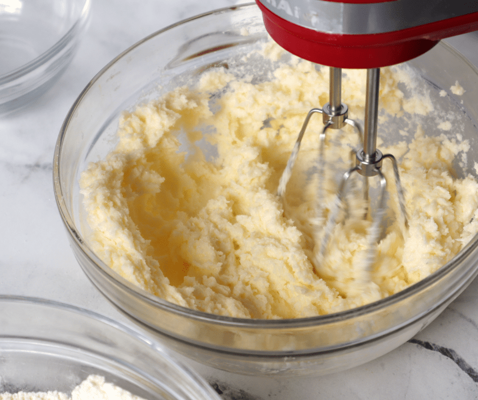 Mixing bowl with fluffy butter and sugar, eggs, applesauce, vanilla, flour, and diced apples being combined for cookie dough.