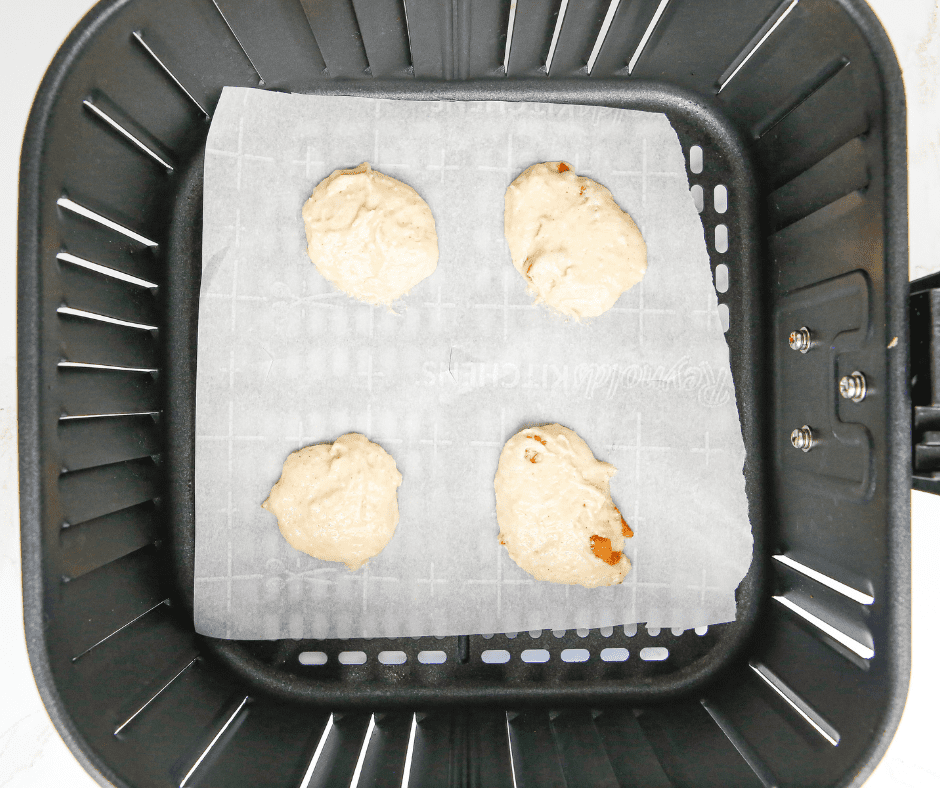 Tablespoons of apple pie spice cookie batter dropped onto parchment paper in an air fryer basket, ready to cook.