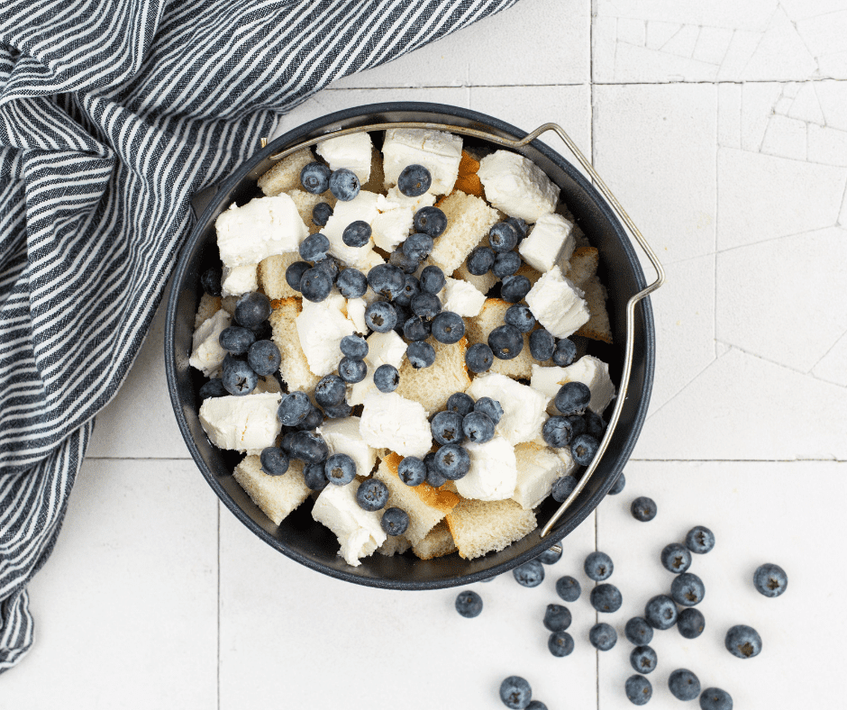 Baking pan sprayed with cooking spray, filled with bread cubes, cream cheese, and blueberries