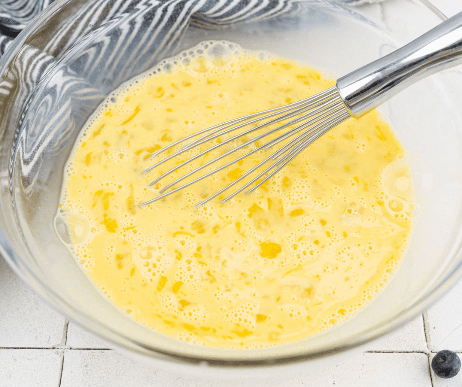 Large mixing bowl with eggs, milk, vanilla, and maple syrup being poured over bread mixture
