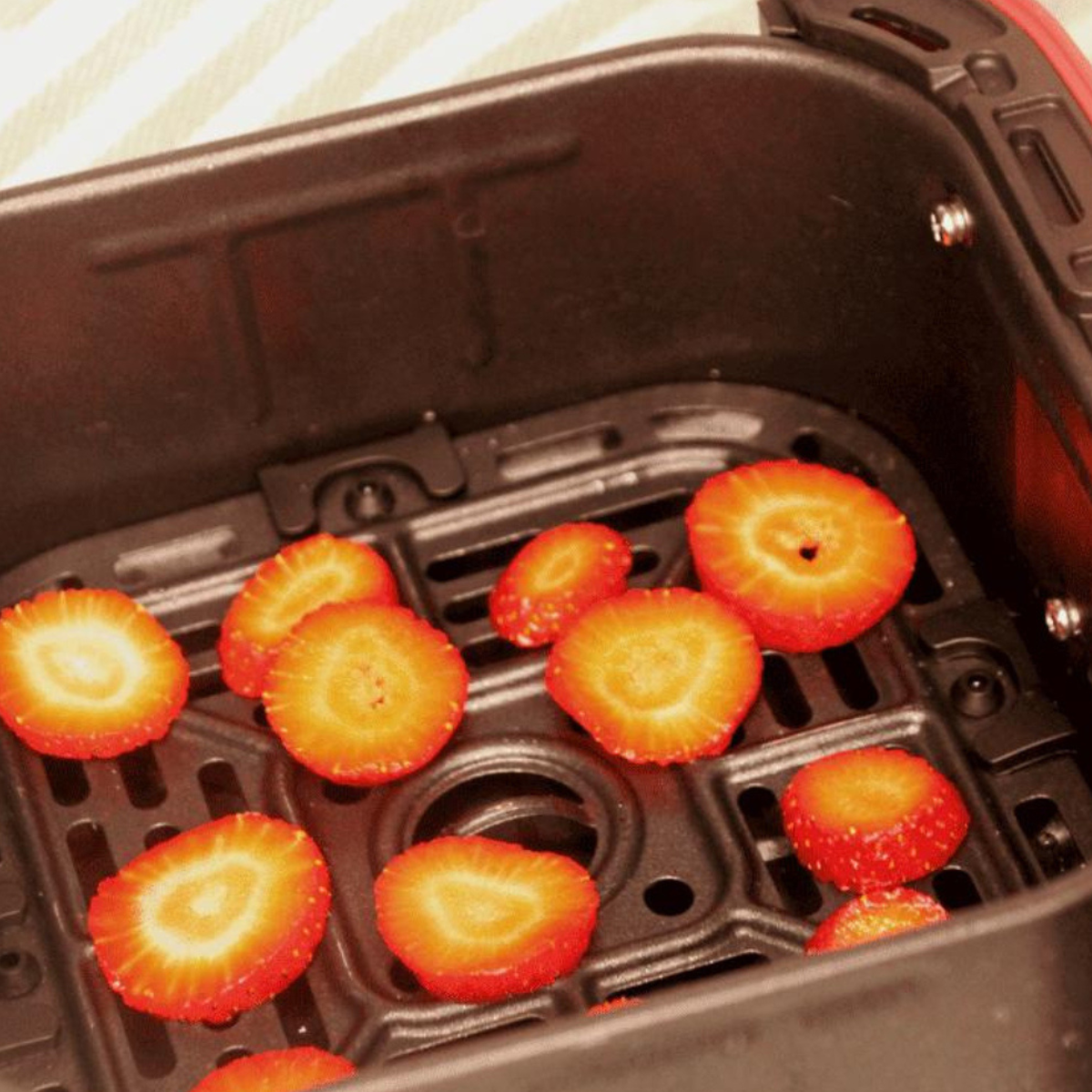 Air fryer with sliced strawberries inside, demonstrating the dehydrating process.