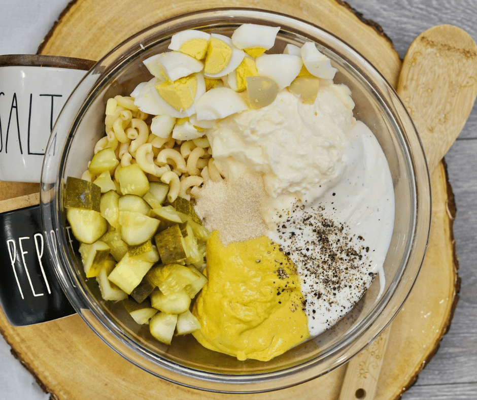 Creamy deviled egg pasta salad in mixing bowl with macaroni, mayo, ranch dressing, mustard, chopped eggs, and pickles being mixed together.