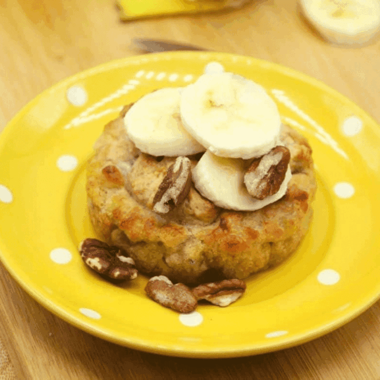 A fluffy, golden-brown banana bread mug cake inside a ceramic ramekin, topped with a few banana slices and a sprinkle of cinnamon.