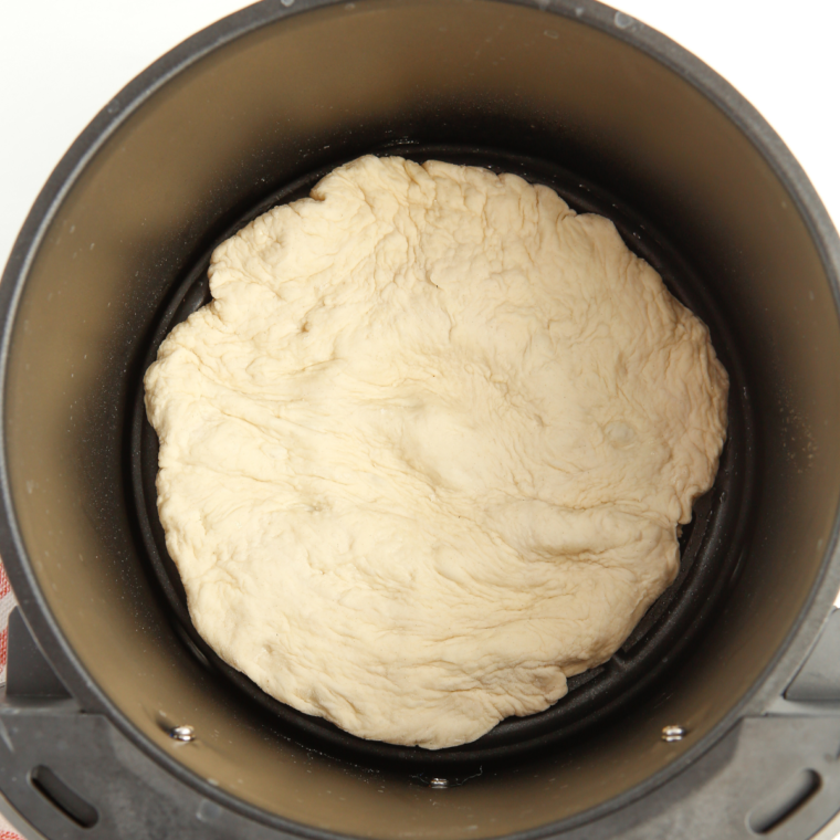 Pizza dough rolled into a round on a floured surface, sized for the air fryer basket