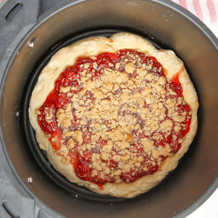 Cherry dessert pizza in the air fryer basket topped with cherry filling and streusel before cooking
