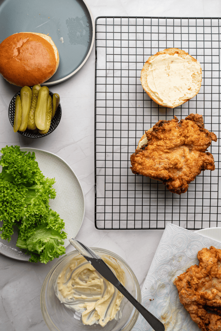 Assembling the sandwich with crispy chicken, lettuce, tomato, pickles, and sauce.