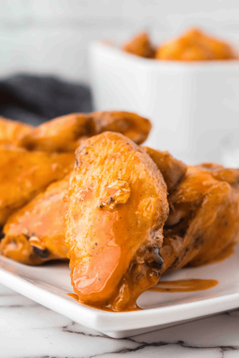Crispy, golden chicken wings coated in spicy buffalo sauce, served on a plate with dipping sauce.