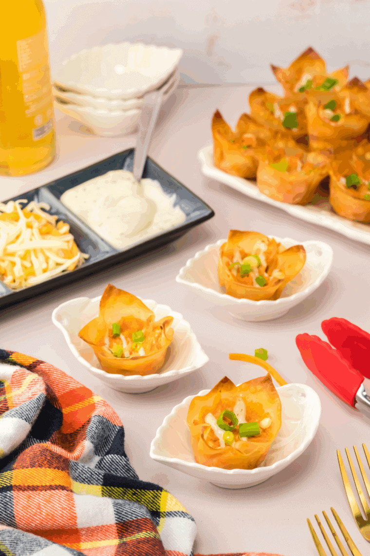 Crispy air fryer buffalo chicken wontons stacked on a plate, served with ranch and garnished with green onions, ready to enjoy.