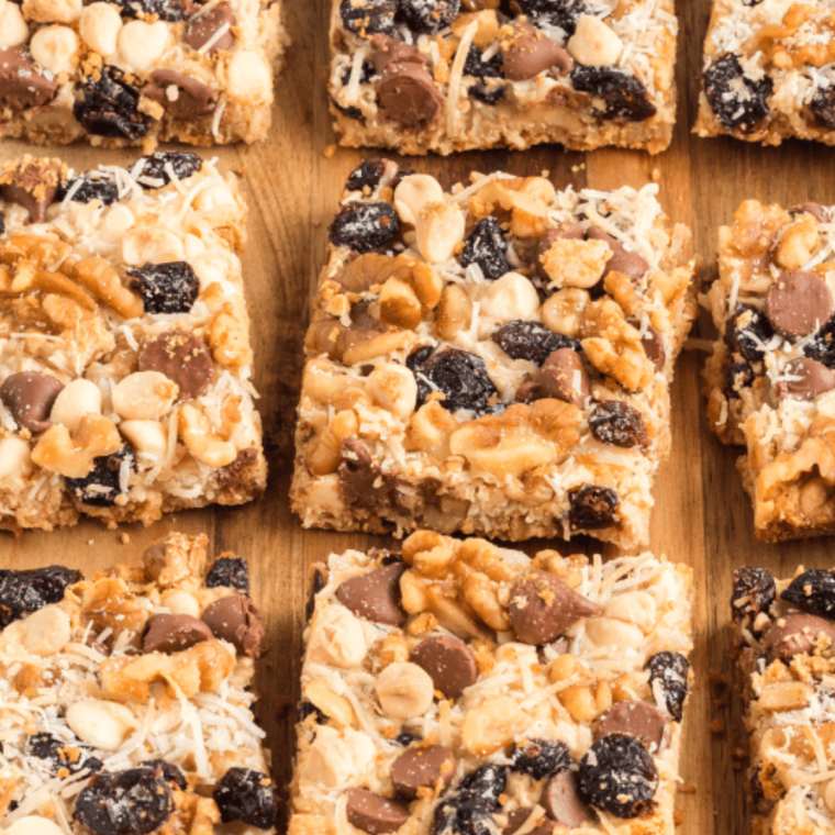 A close-up shot of sliced Cranberry Magic Cookie Bars showing thick layers of graham cracker crust, melted white chocolate, vibrant red dried cranberries, and golden toasted shredded coconut.