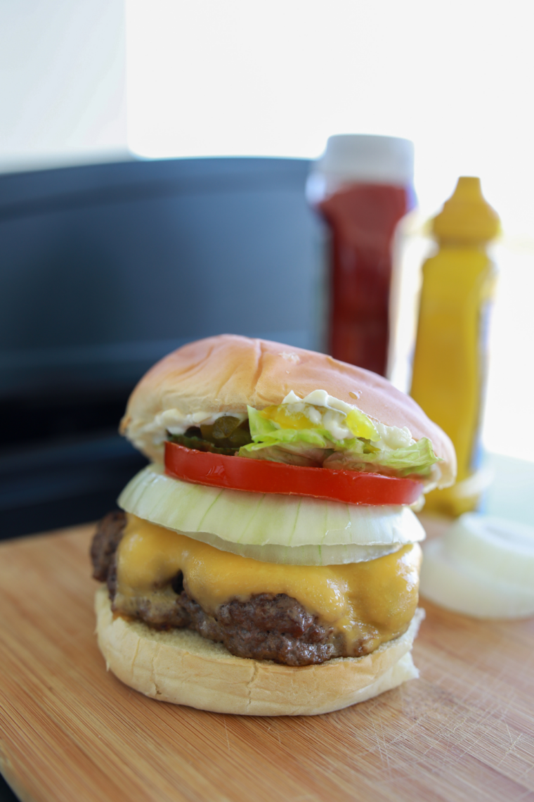 Homemade frozen hamburgers cooked on a Blackstone griddle with crispy edges and melted cheddar cheese