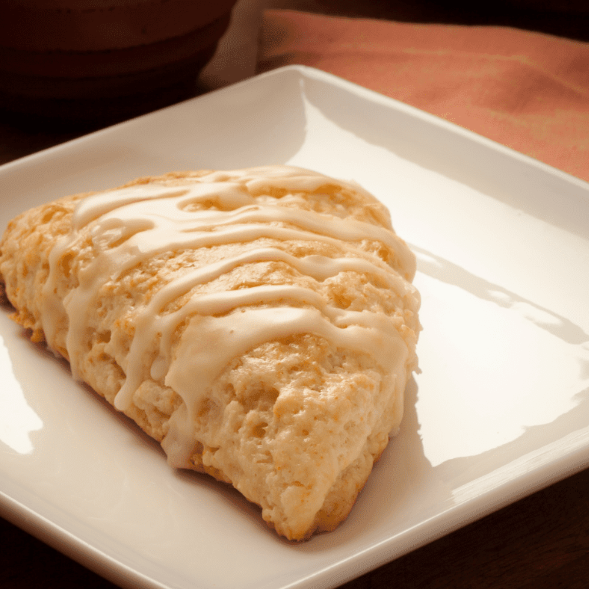 Golden air fryer scones being drizzled with sweet vanilla bean glaze in the basket