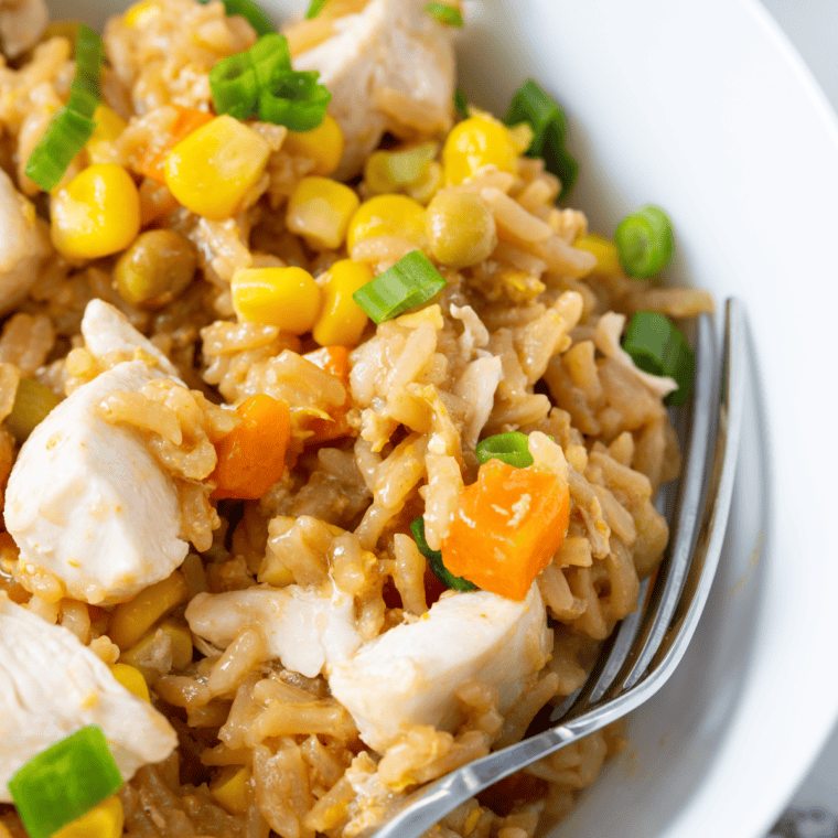A bowl of homemade Panda Express fried rice with eggs, peas, carrots, and green onions, served on a white plate.