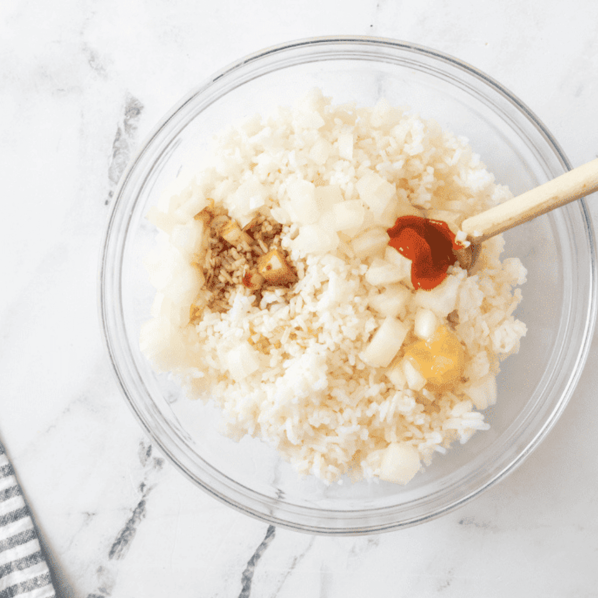 A large bowl with cold cooked rice, oil, and soy sauce being mixed together.