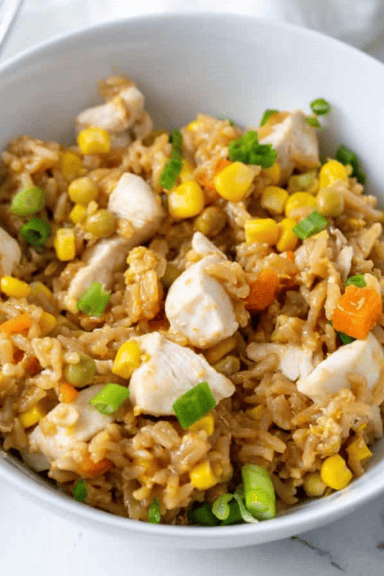A bowl of homemade Panda Express fried rice with eggs, peas, carrots, and green onions, served in a white bowl.